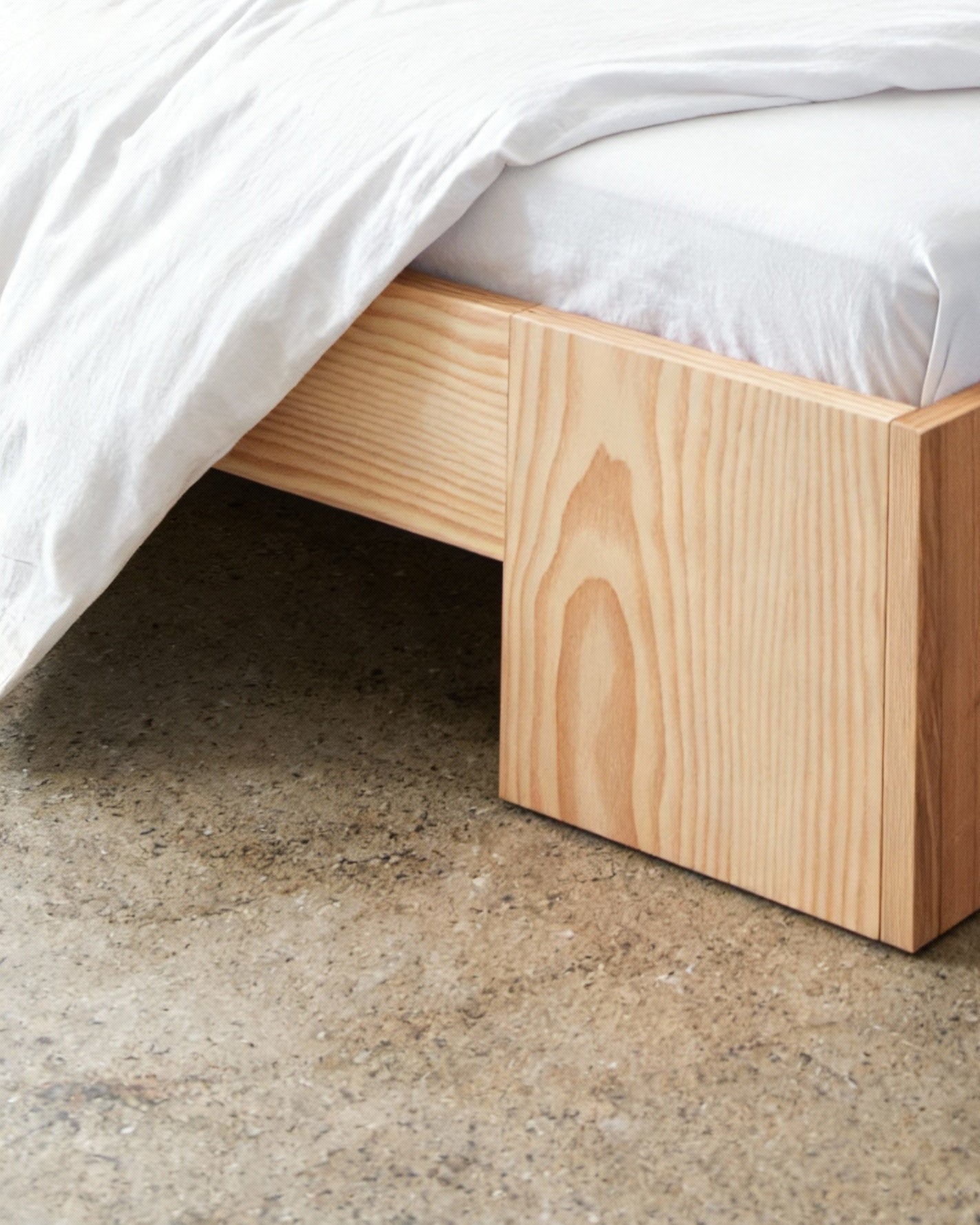 Wooden bed frame with white bedding on a concrete floor