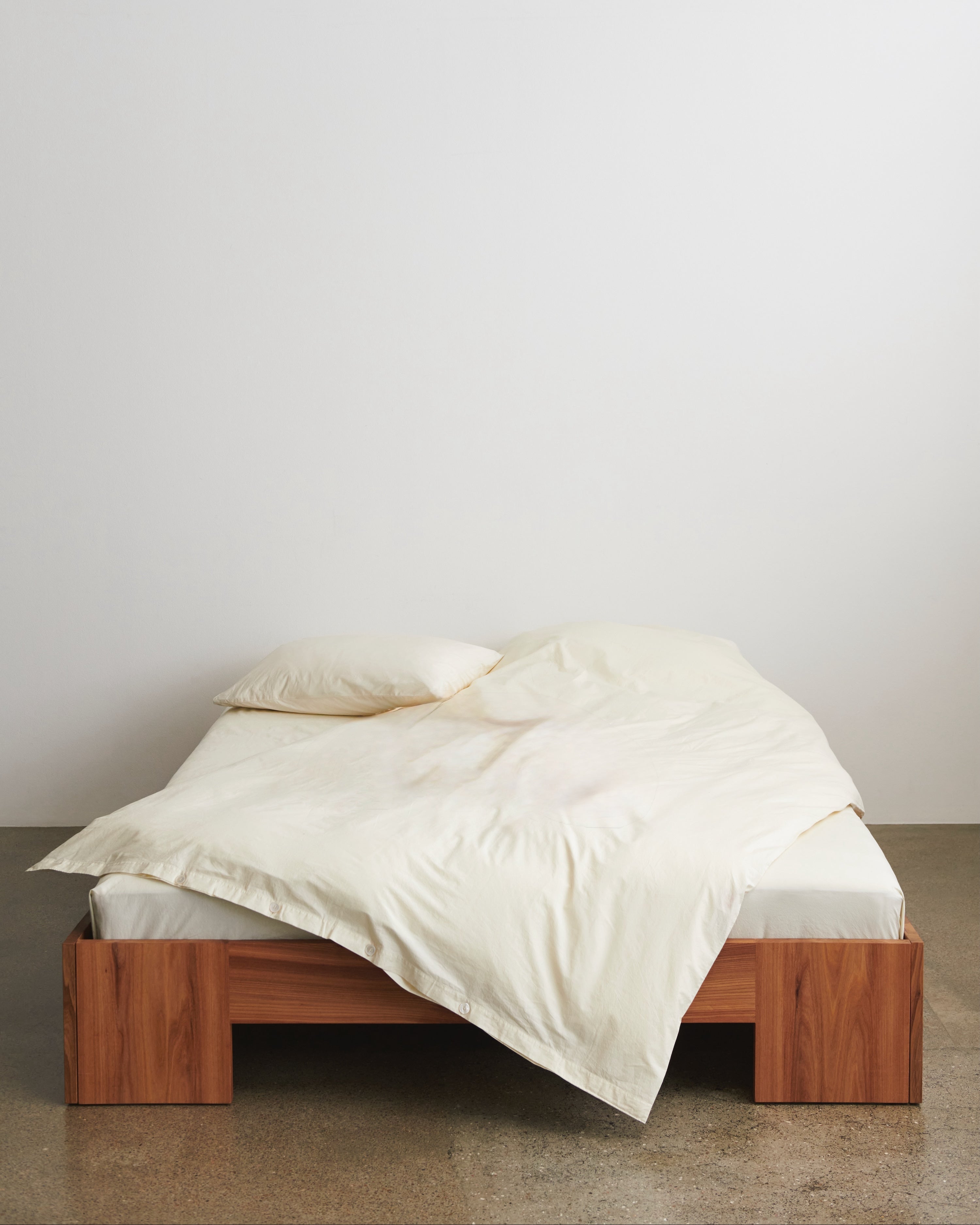 Wooden bed frame with white bedding against a plain wall