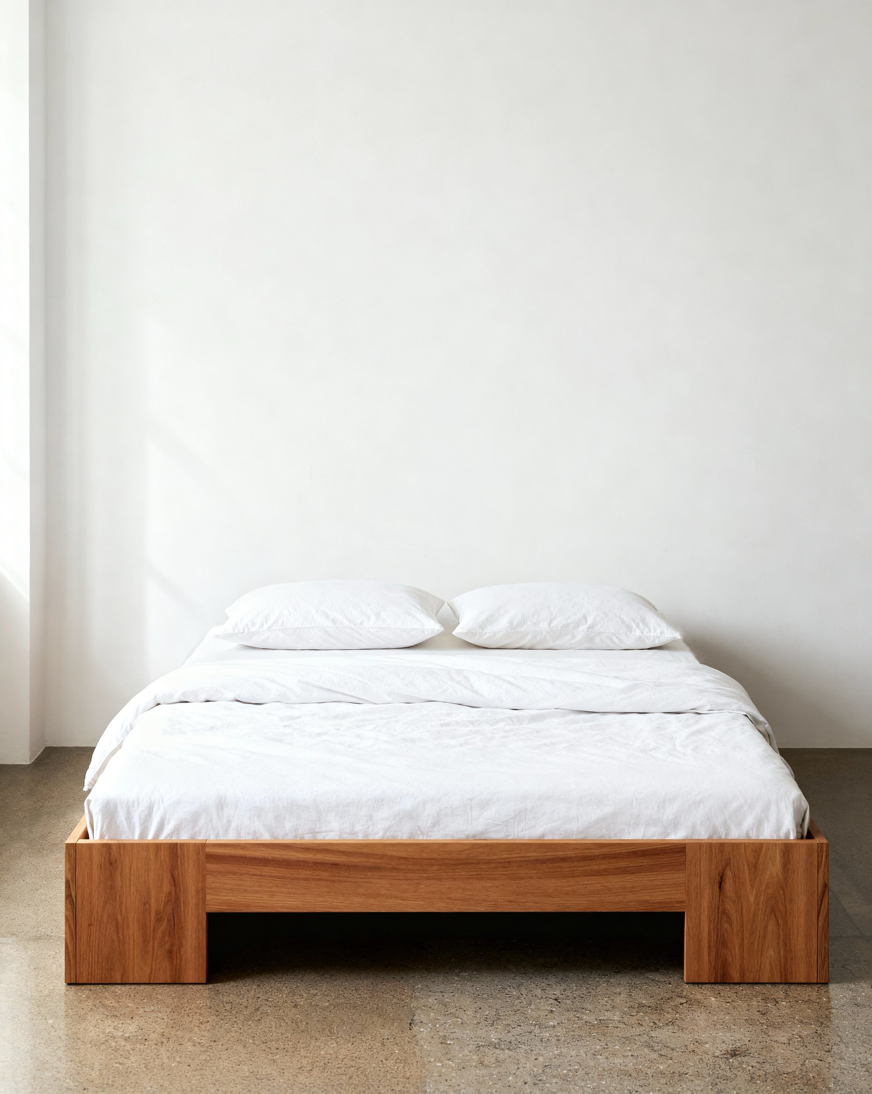 Wooden bed frame with white bedding against a plain wall